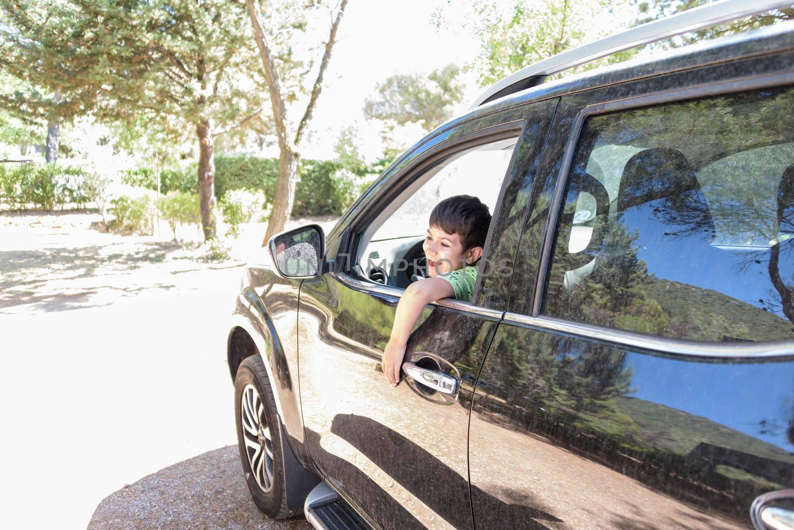 laughing boy looking out of car window. happy child in the back seat of the car enjoying the view from the window. The concept of freedom, school vacations or holidays