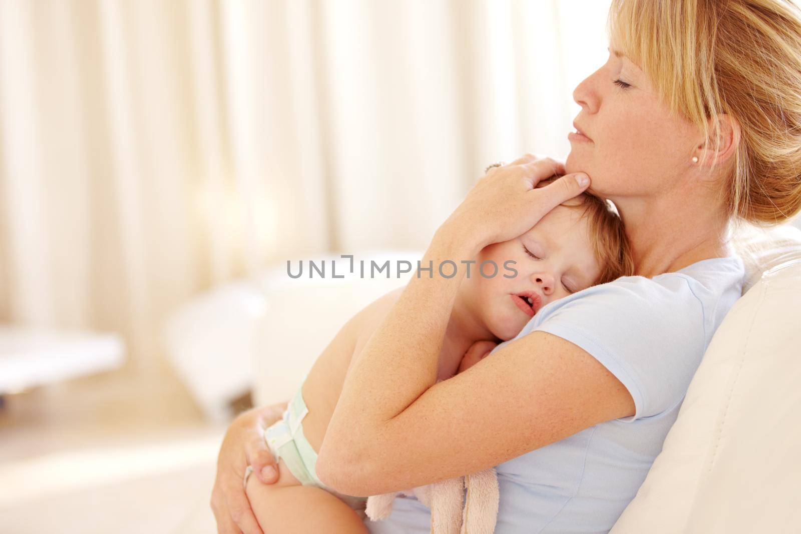 Beautiful woman cradling her sleeping baby to her chest on the couch at home.