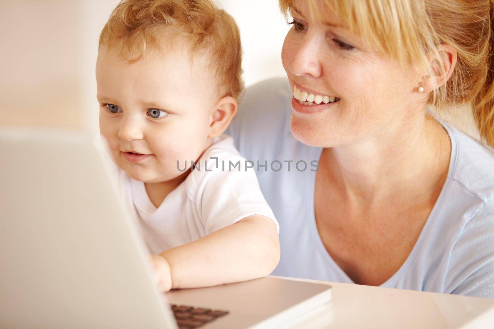 Beautiful mother helping her little baby boy type on her laptop computer.
