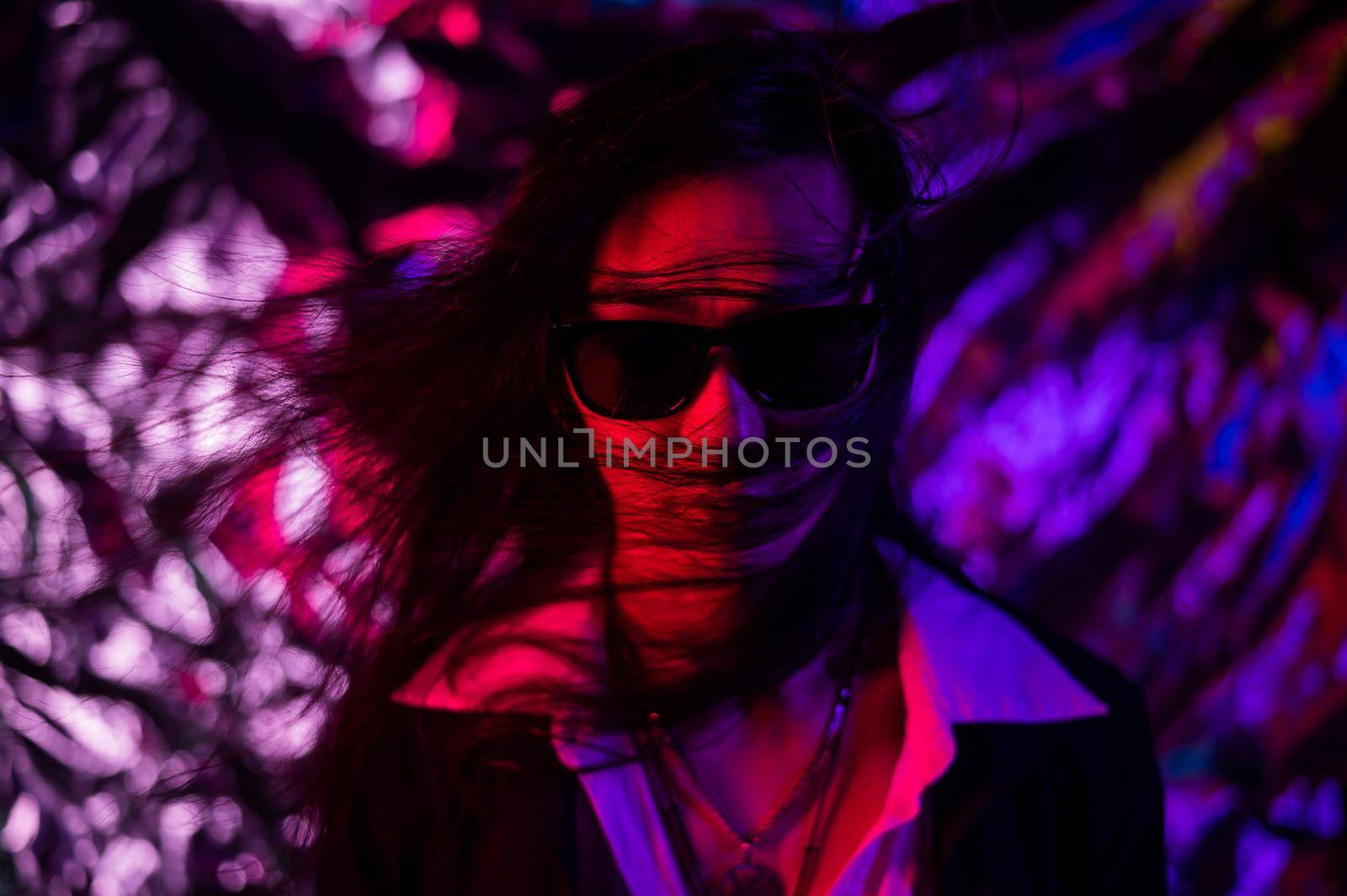 Portrait of a transgender model in sunglasses in a studio with neon lighting