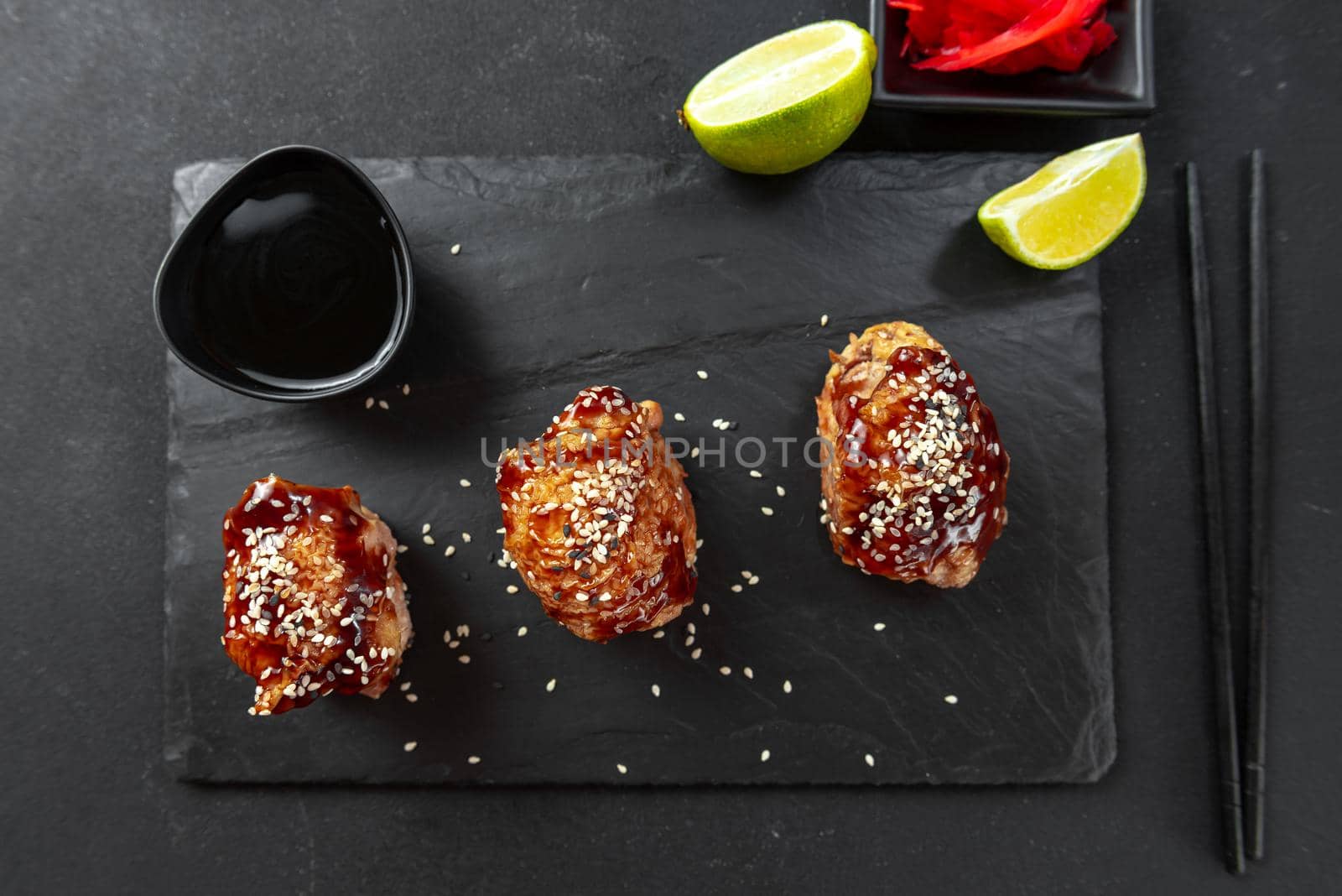 Asian appetizer. Chinese cuisine chicken in sweet and sour sauce on a black background. Chicken with teriyaki sauce and sesame seeds. Next to it are chopsticks and soy sauce by gulyaevstudio
