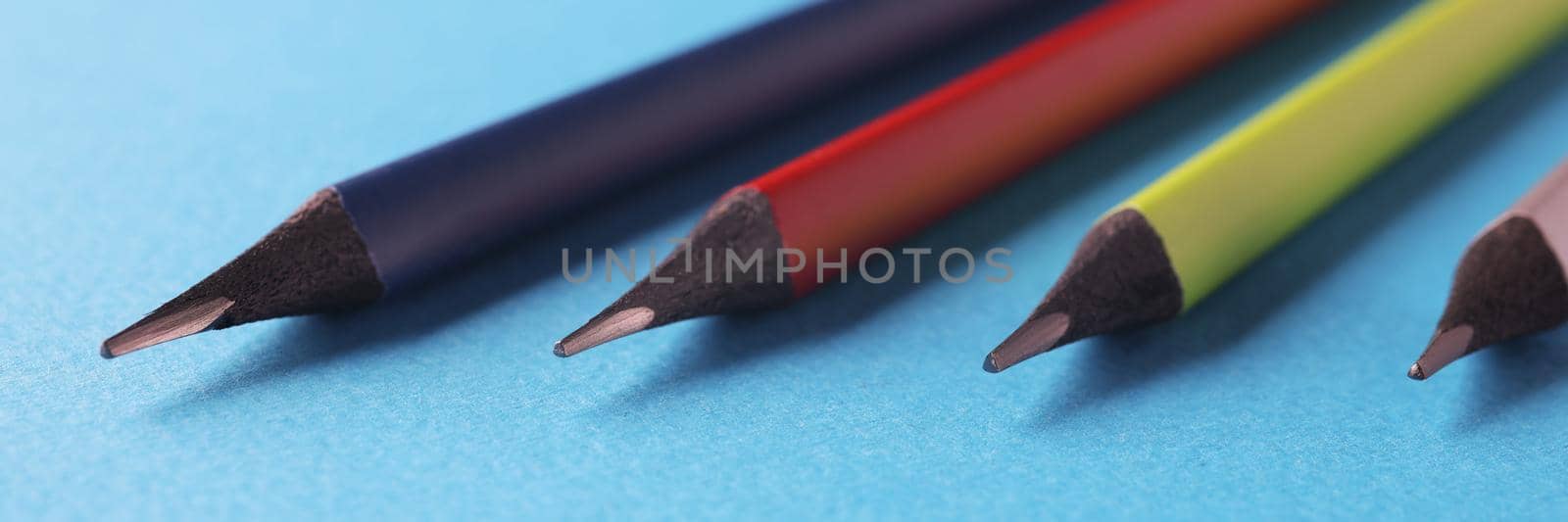 Close-up of colored pencils arranged in decreasing size order on blue surface. Equipment for drawing your dreams, ideas and vision. Art, creativity concept