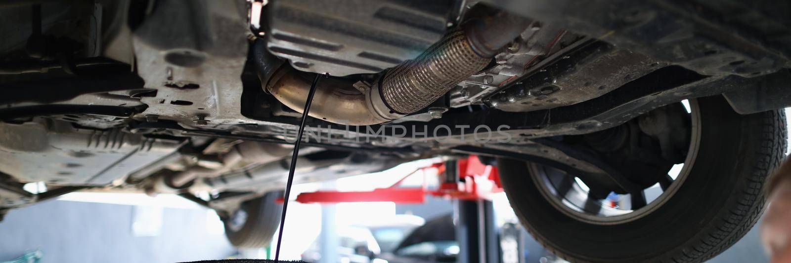 Close-up of automobile lifted in air dripping oil in container, worker control process. Professional car maintenance in service centre. Pit stop concept