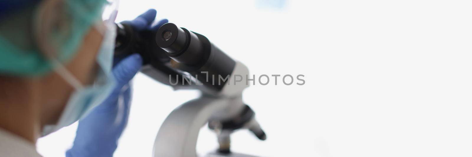 Woman chemist in blue protective glove look at microscope in chemistry lab by kuprevich