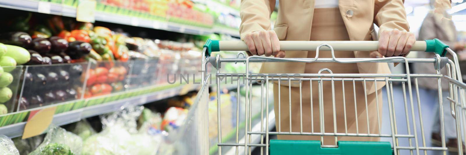 Portrait of smiling woman with shopping cart in supermarket buying groceries food walking along aisle and shelves in grocery store. Shopping, food concept