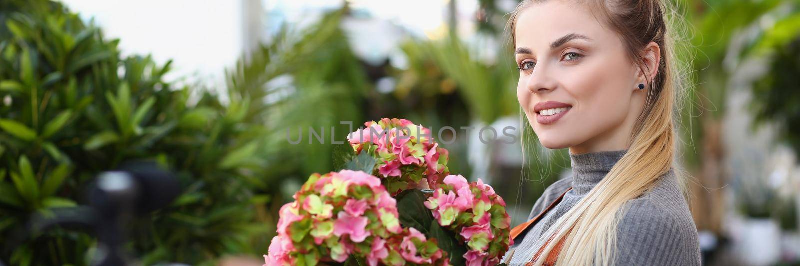 Portrait of beautiful blonde florist studio worker record promotion for botanical store. Female posing with fresh blooming flowers. Shop, sell, ad concept