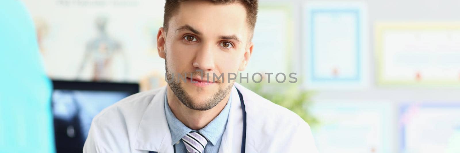 Portrait of attractive young medical worker in white uniform, wait patient for planned appointment. Young specialist in medicine. Healthcare, help concept