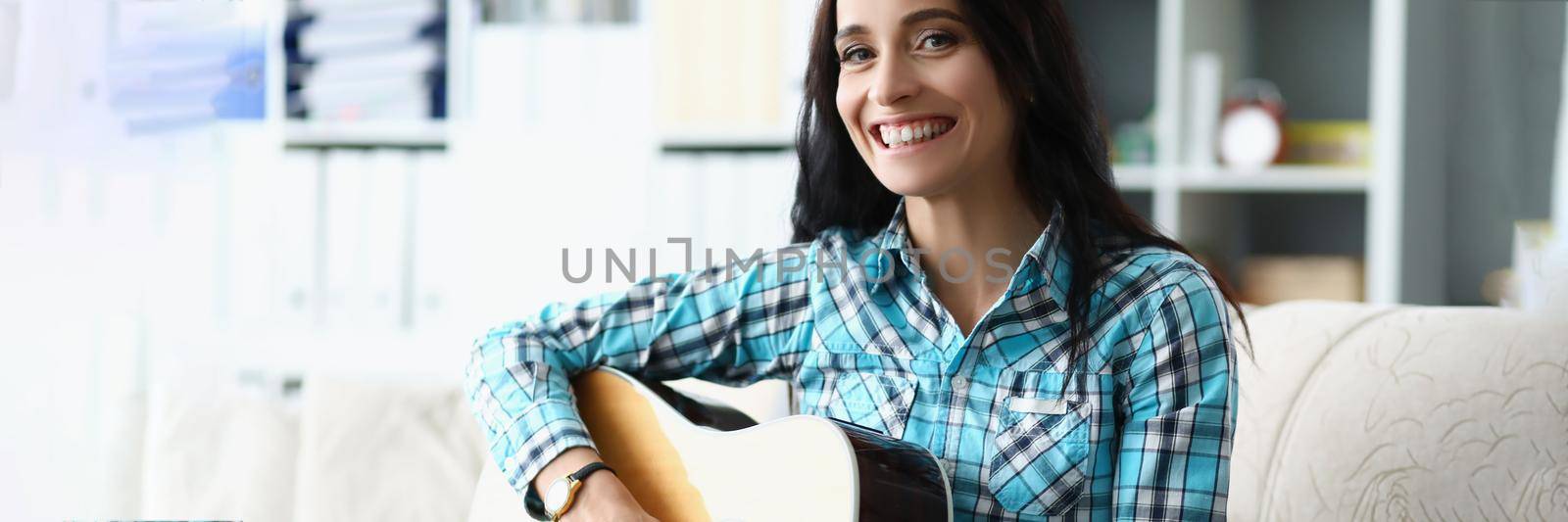 Portrait of happy young woman playing on guitar in living room at home, spend free time learning new song on musical instrument. Music, hobby, joy concept