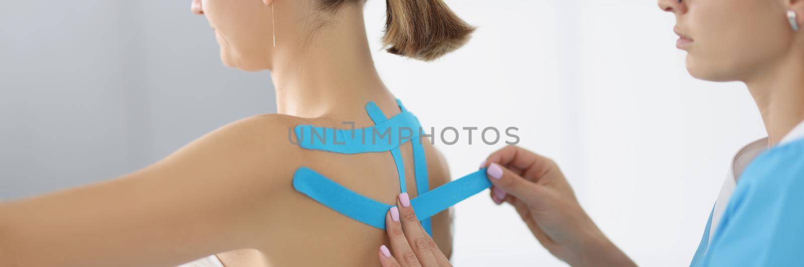 Portrait of doctor apply kinesiology tape on patient back in clinic. Procedure on recovering after injury. Rehabilitation room, healthcare, therapy concept