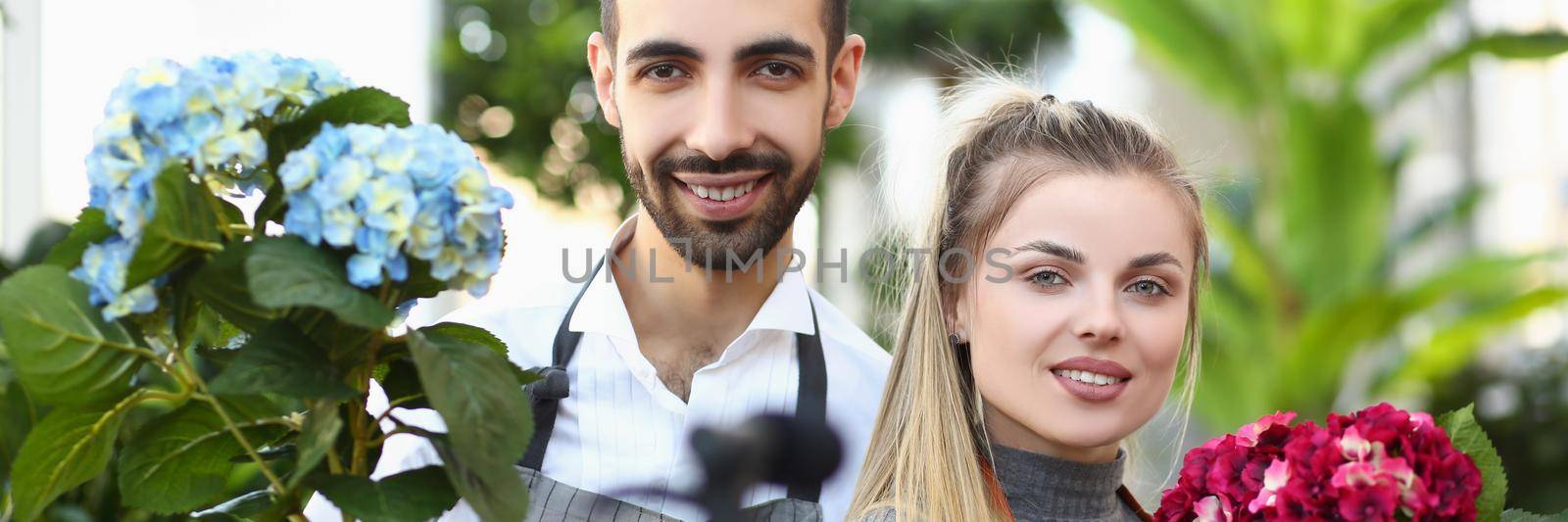 Portrait of young woman and man posing for picture with luxury bouquets of flowers. Smiling workers present their product from shop. Ad, business concept