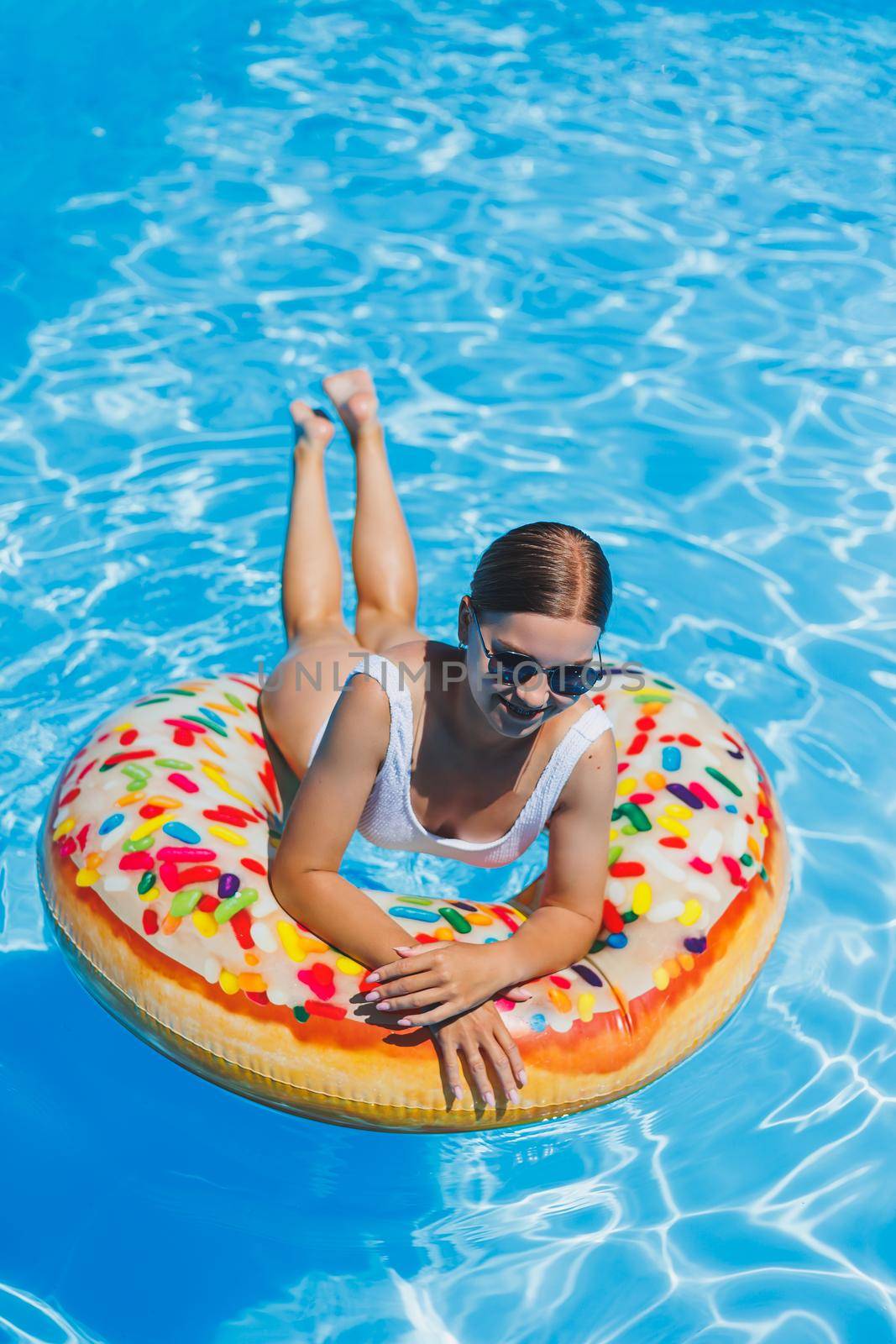 Rest in the pool. Happy young woman in swimsuit, sunglasses and inflatable rubber ring floating in blue water. Summer luxury holidays in the spa resort pool