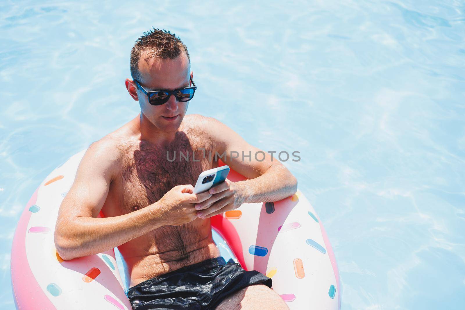 An attractive man is relaxing on an inflatable ring in the pool. A man in the pool is talking on the phone. vacation and free time concept by Dmitrytph