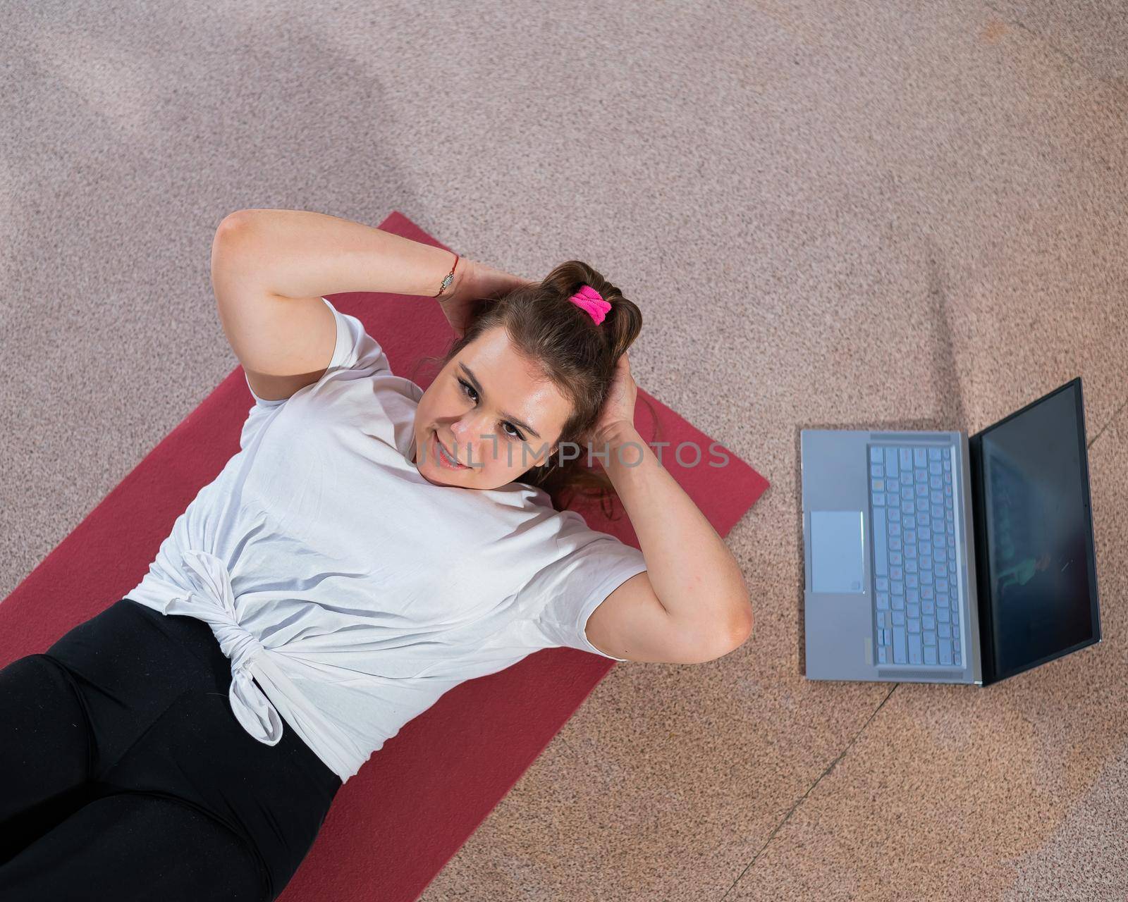 A chubby young woman is watching an online fitness lesson on a laptop. Distance sports training. by mrwed54