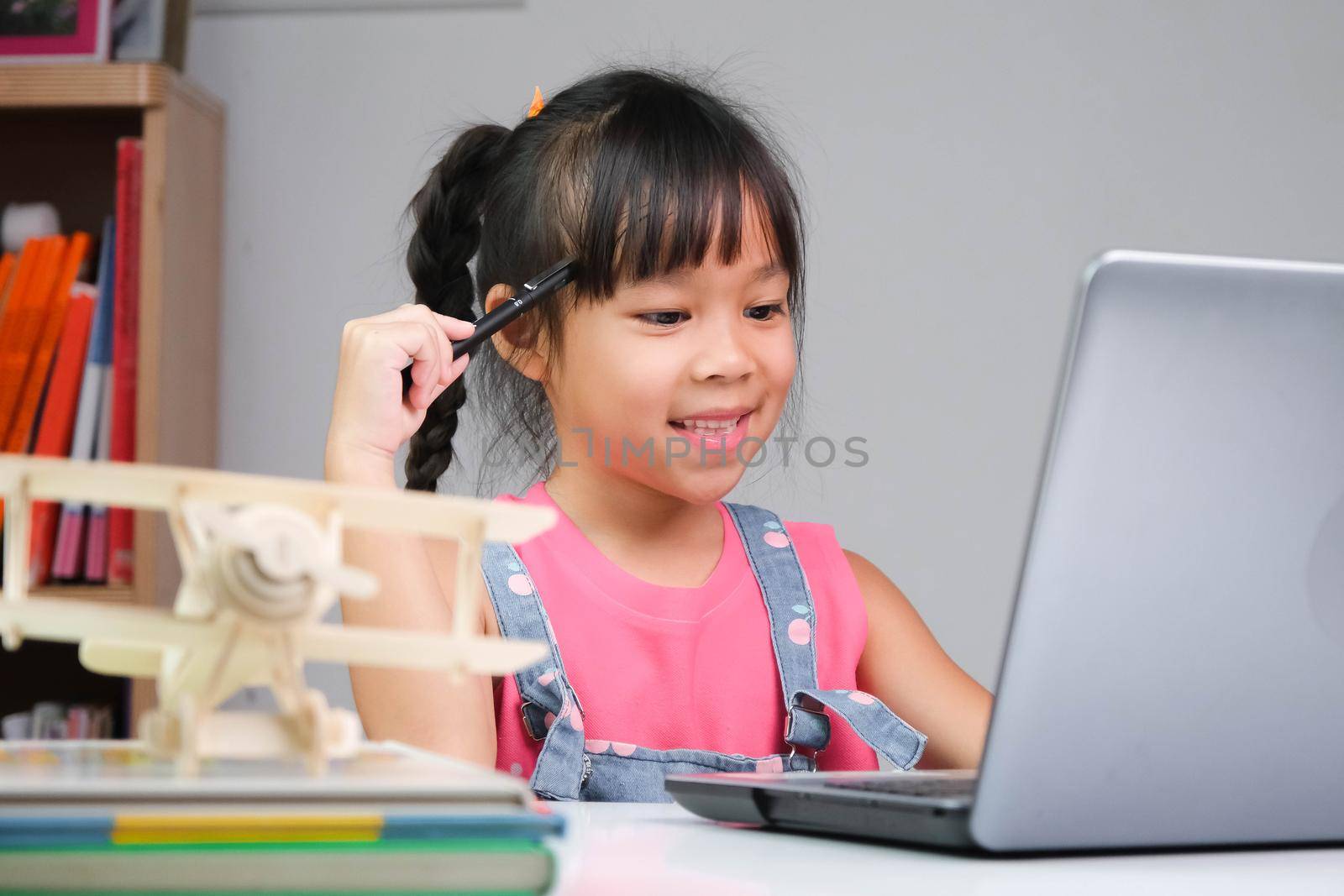 Smiling little Asian girl studying online having video call distant class with teacher using laptop. Happy girl learning English online with laptop at home. homeschooling concept