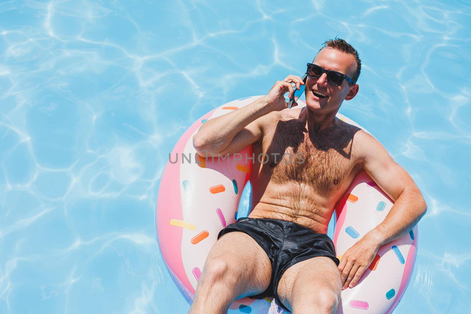 An attractive man is relaxing on an inflatable ring in the pool. A man in the pool is talking on the phone. vacation and free time concept by Dmitrytph