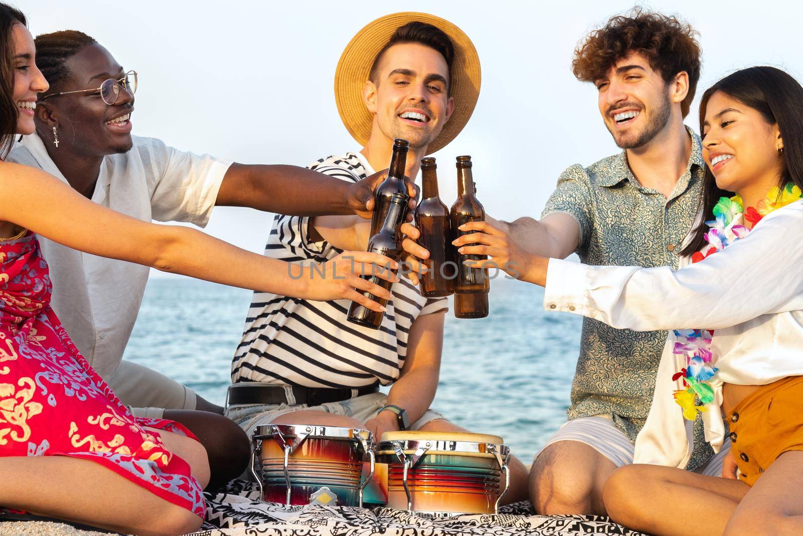 Cheers. Smiling friends enjoy some cold beer at the beach. Diverse happy young people toasting with beer outdoors. Vacation and friendship concept.