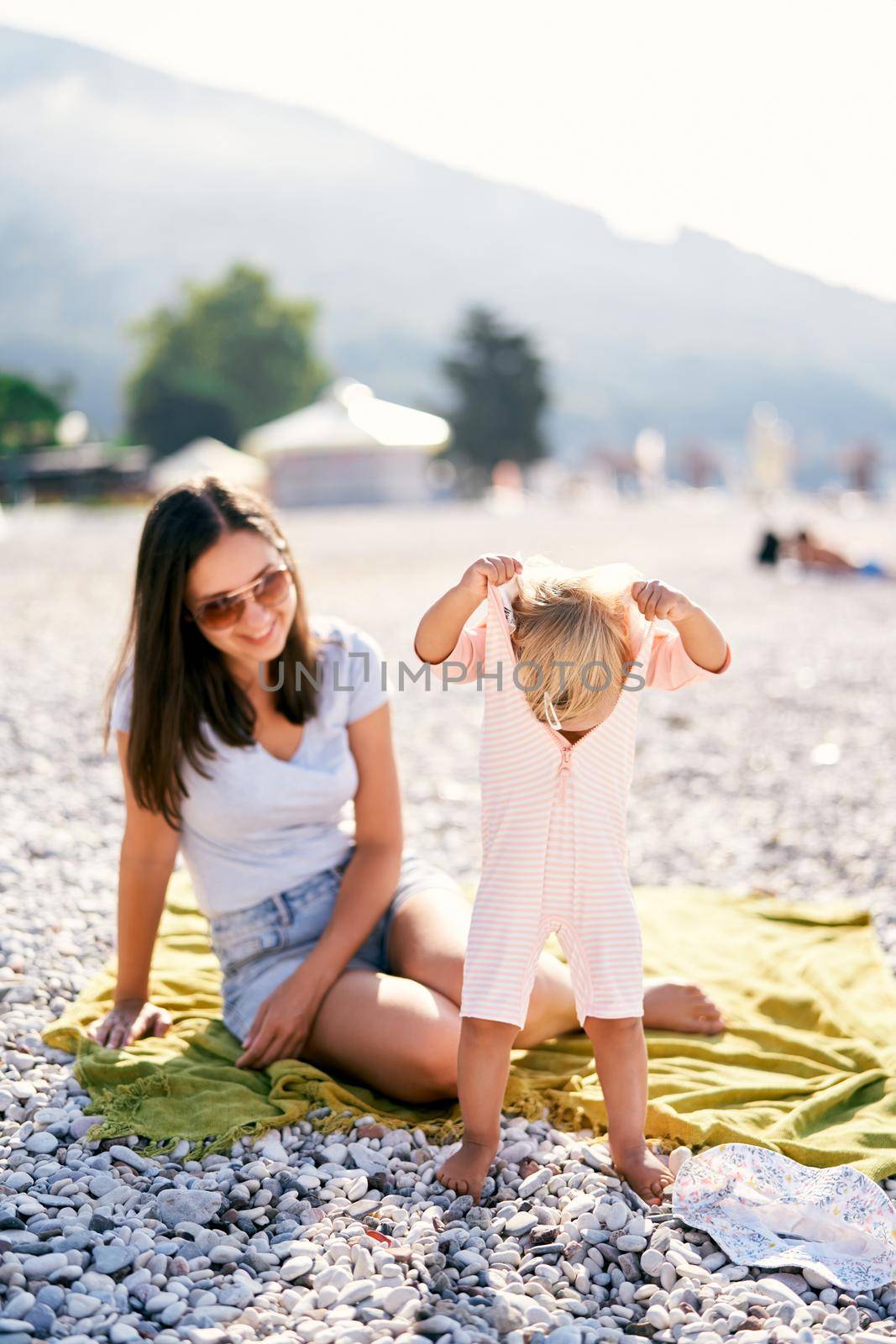 Little girl pulls off overalls while standing on the beach. High quality photo