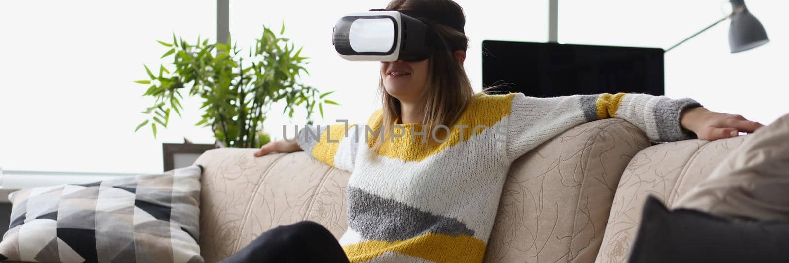 Female sit on couch wear vr glasses modern device at home and enjoy spare time by kuprevich