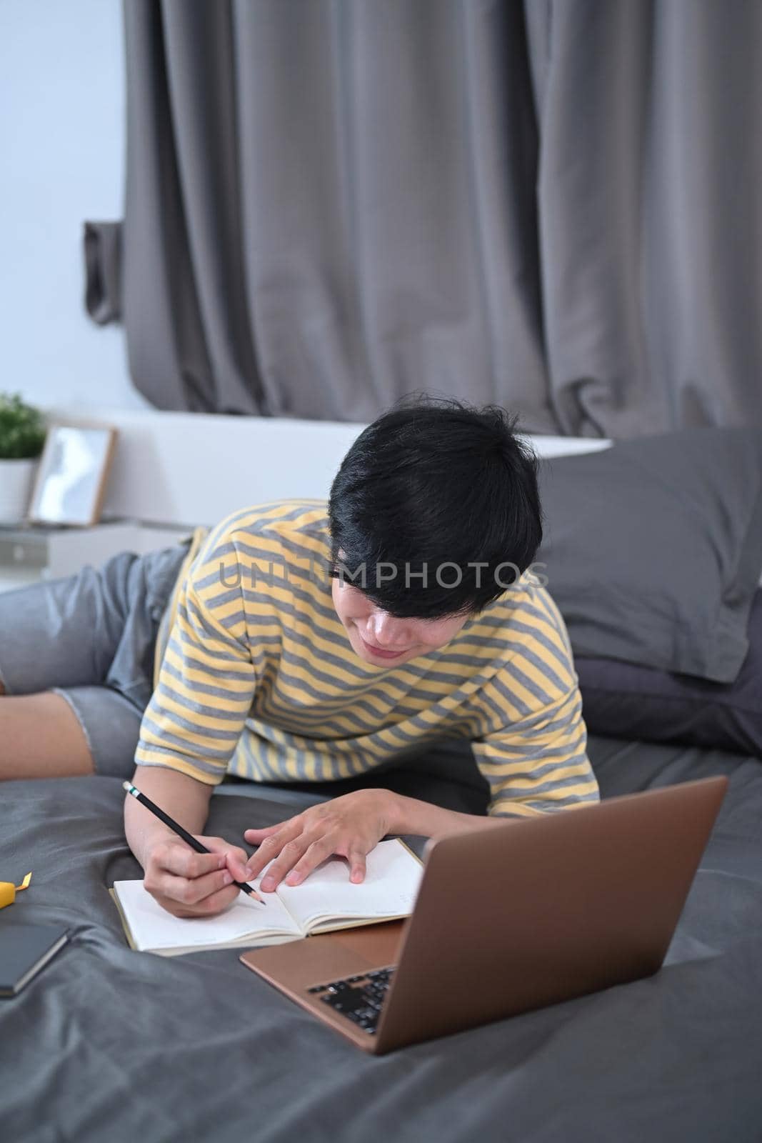 Young man working laptop computer on his bed.