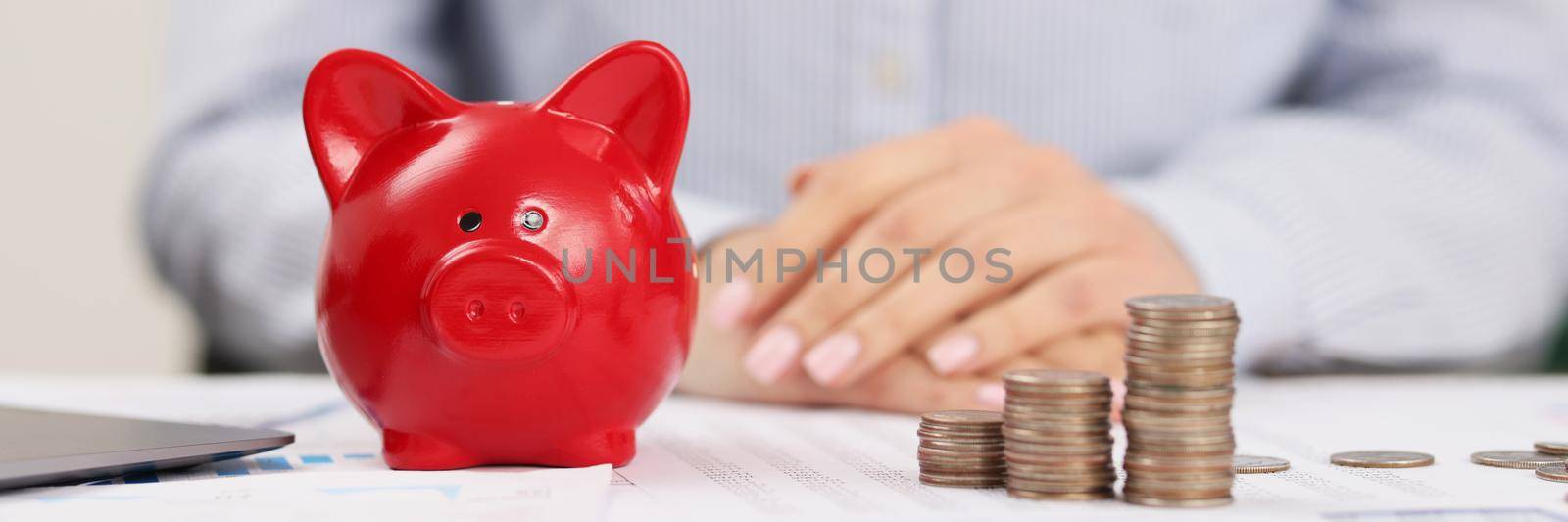 Close-up of person accountant on working place, stack of coins, red piggy bank. Prepare annual report for company on finance. Economy, saving up concept