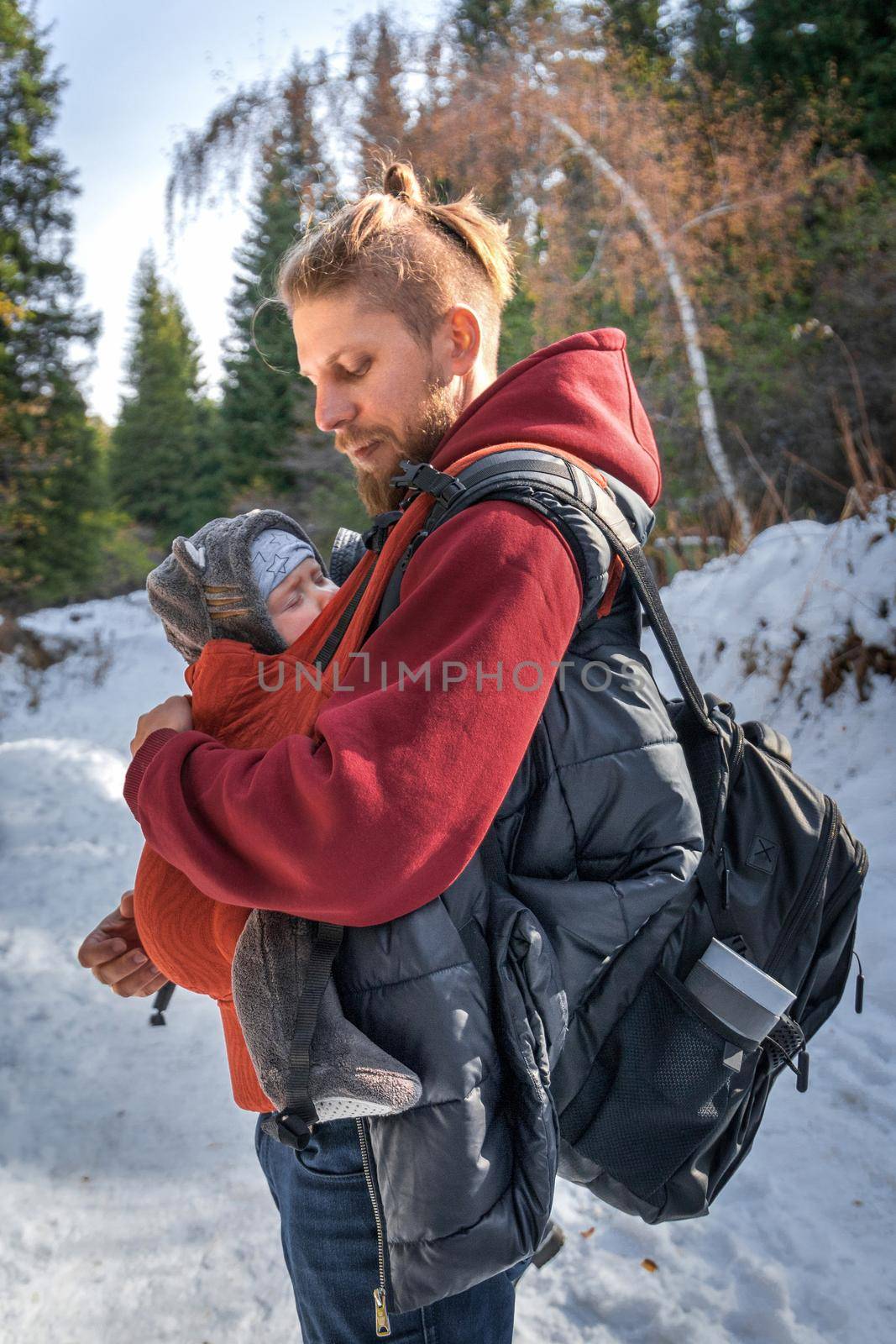 Little boy sleeping in his father's sling while walking in the winter forest.