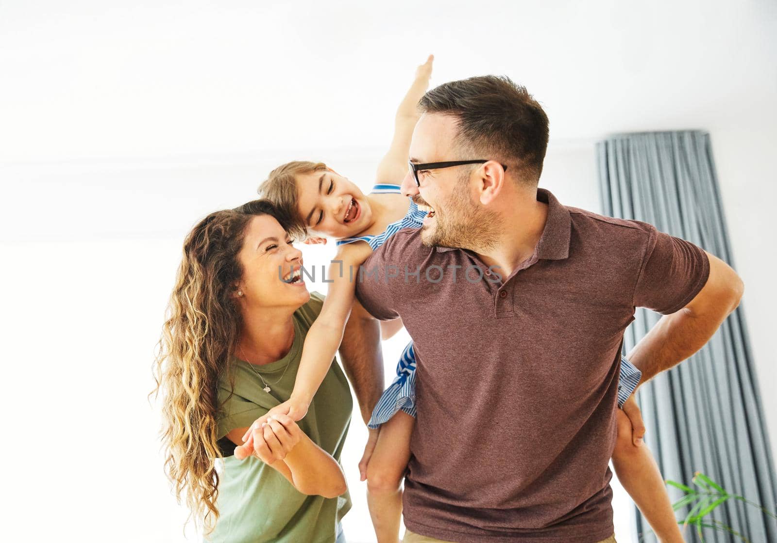 child daughter family happy mother father piggyback playing fun together girl cheerful smiling home indoor by Picsfive