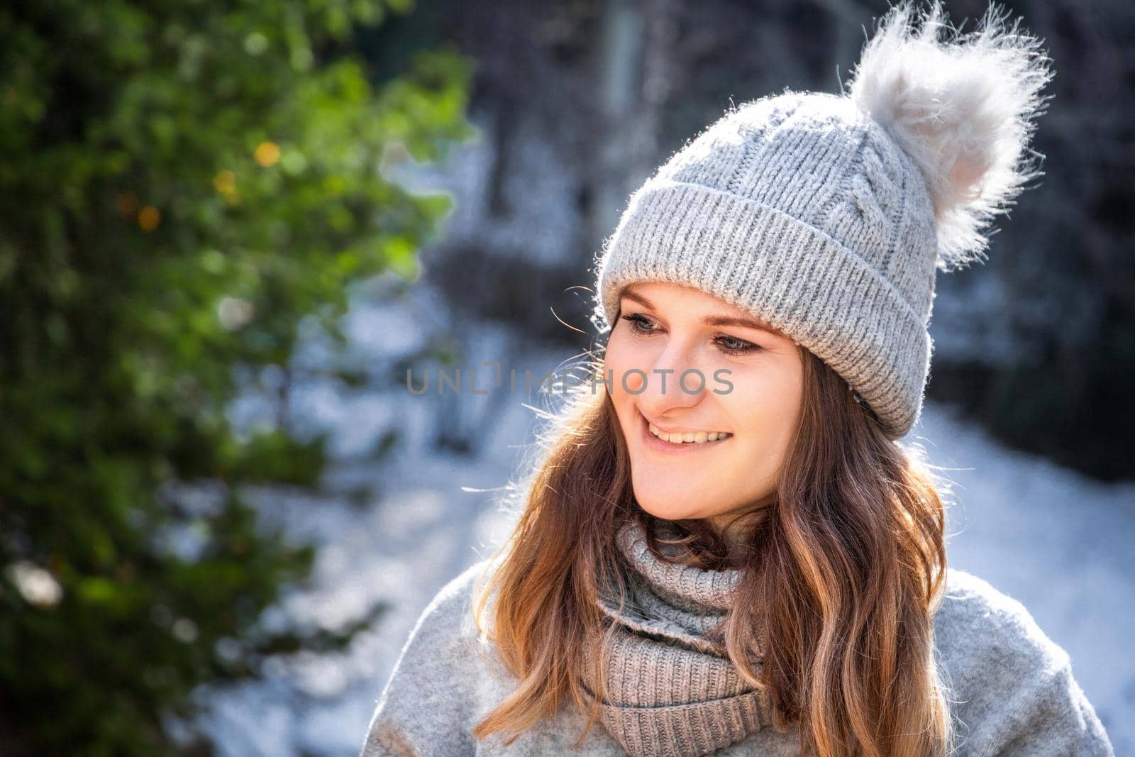 Winter portrait of caucasian blond young smiling woman in grey sweater and beanie hat outdoor.