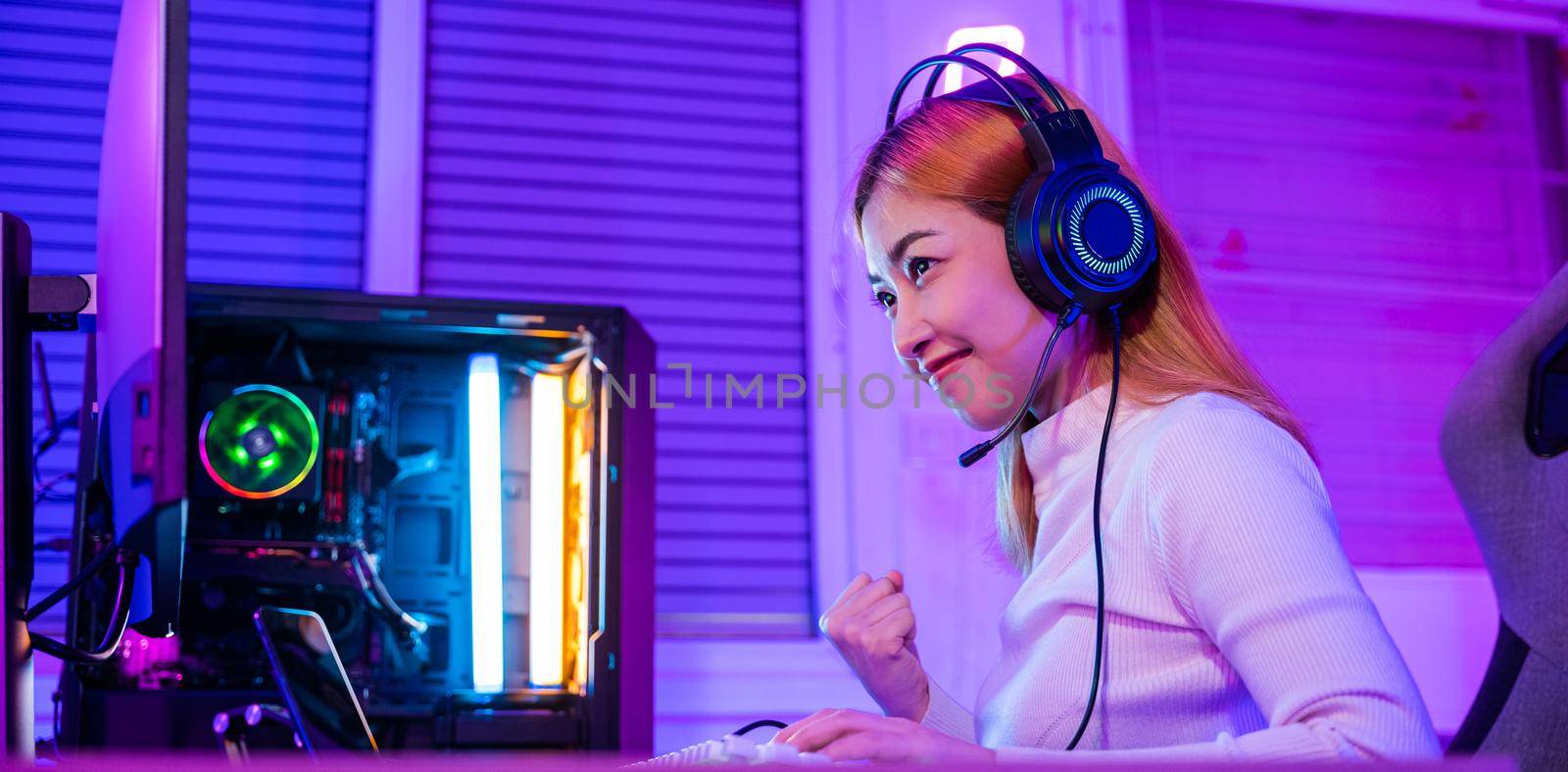 Winning Victory. Asian gamer playing online video game excited on desktop computer PC colorful neon LED lights, young woman in gaming headphones using computer she happy successful, E-Sport concept