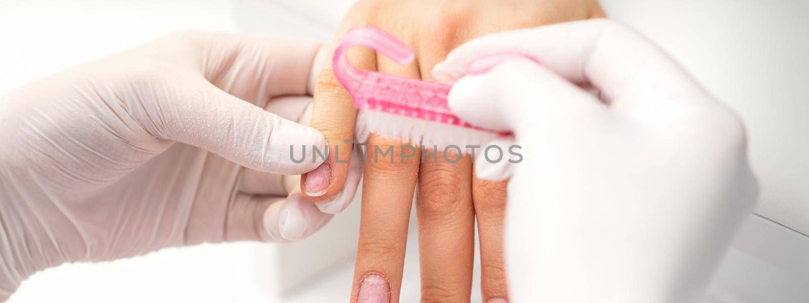 Manicurist cleans dust from the woman's nails with the plastic brush in a nail salon