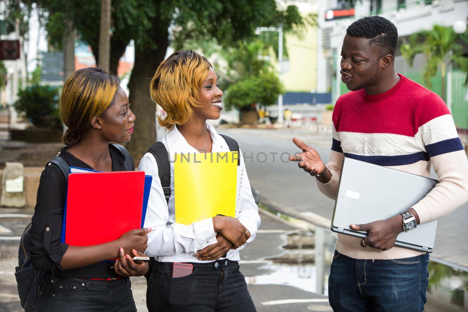 Group of young people with backpacks and notebooks standing and discussing together in the city.