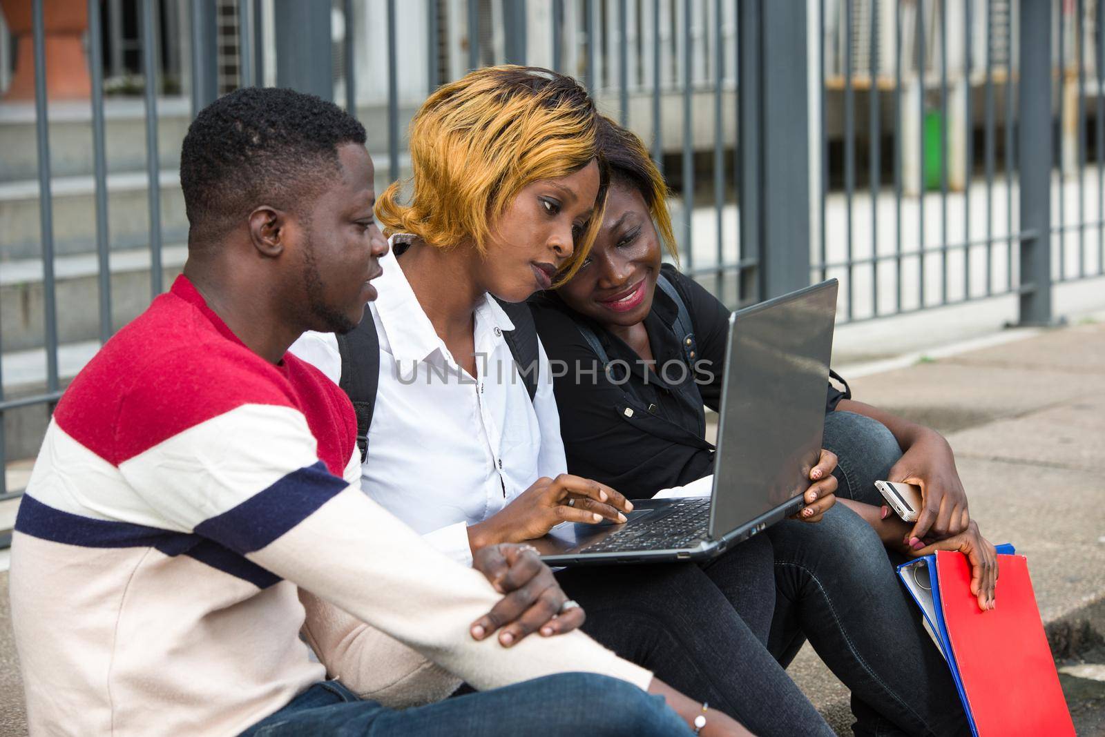 students sitting on the floor looking at laptop smiling.