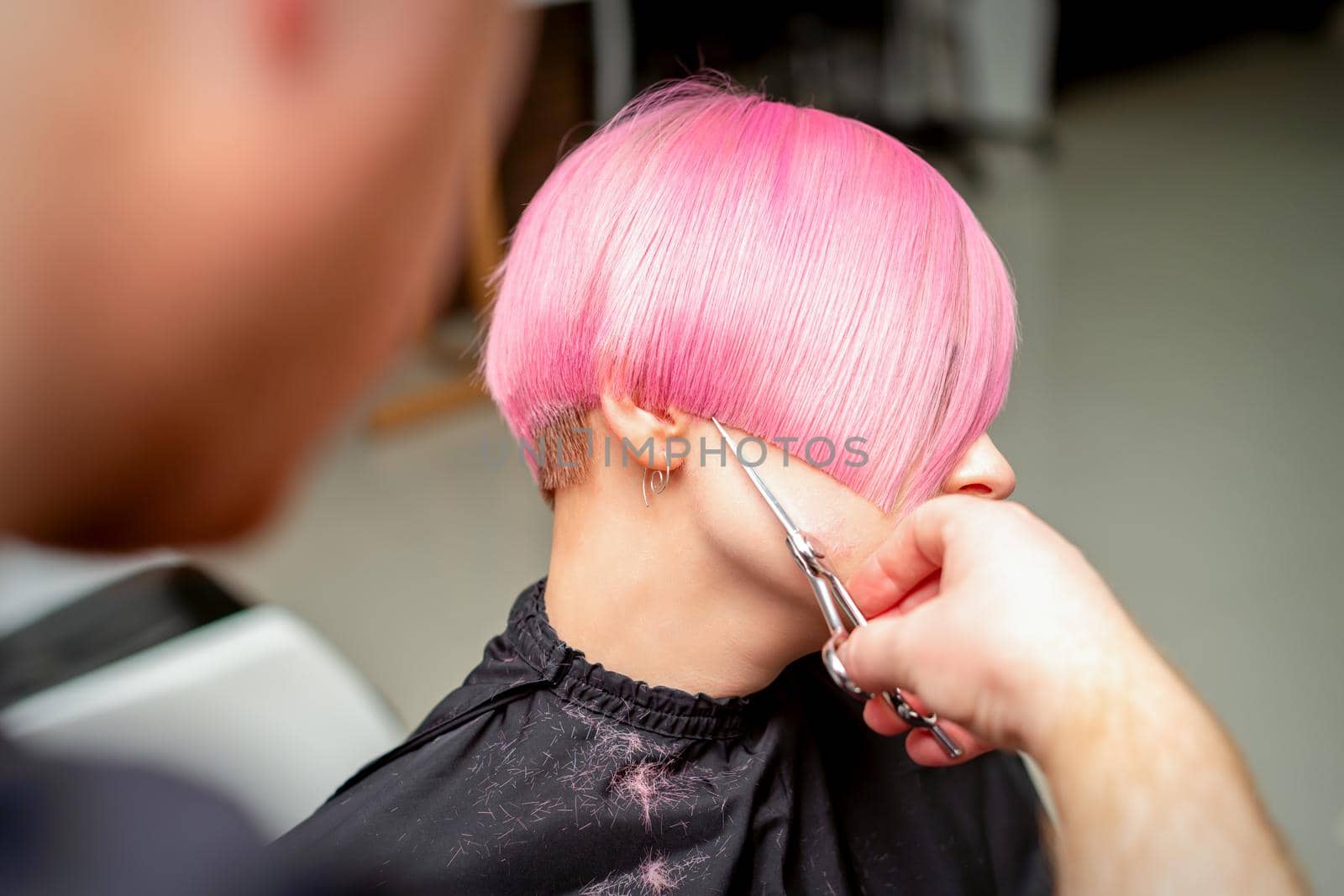 Close up of hairdresser cutting short pink hair of the young woman in a hair salon