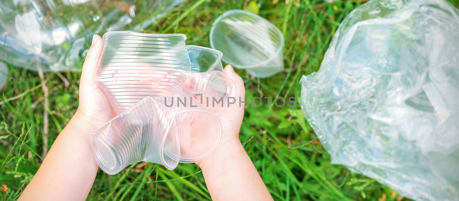 Child's hands clean the park from used plastic utensils in the grass