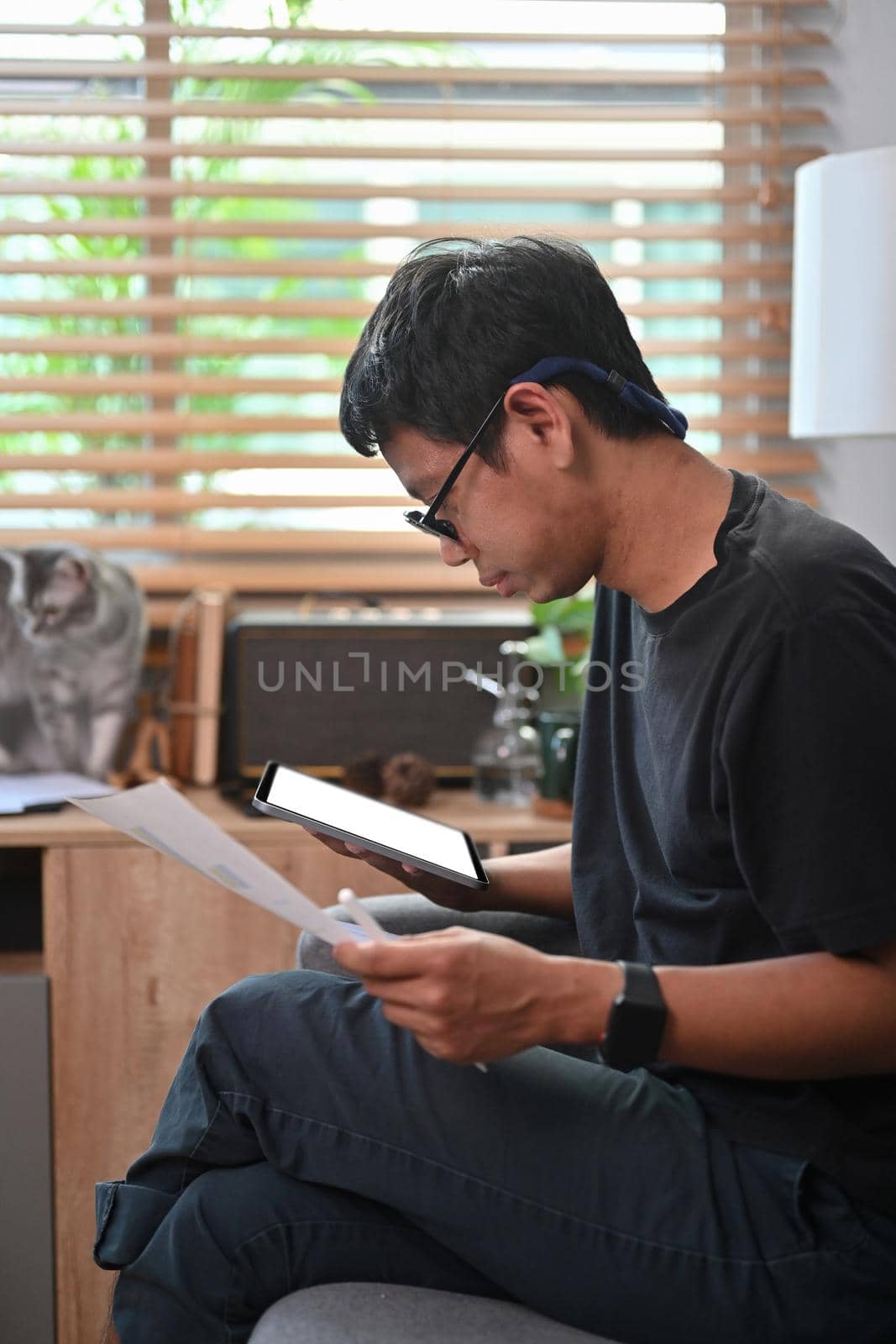 Asian man holding digital tablet and analyzing financial graph at home.