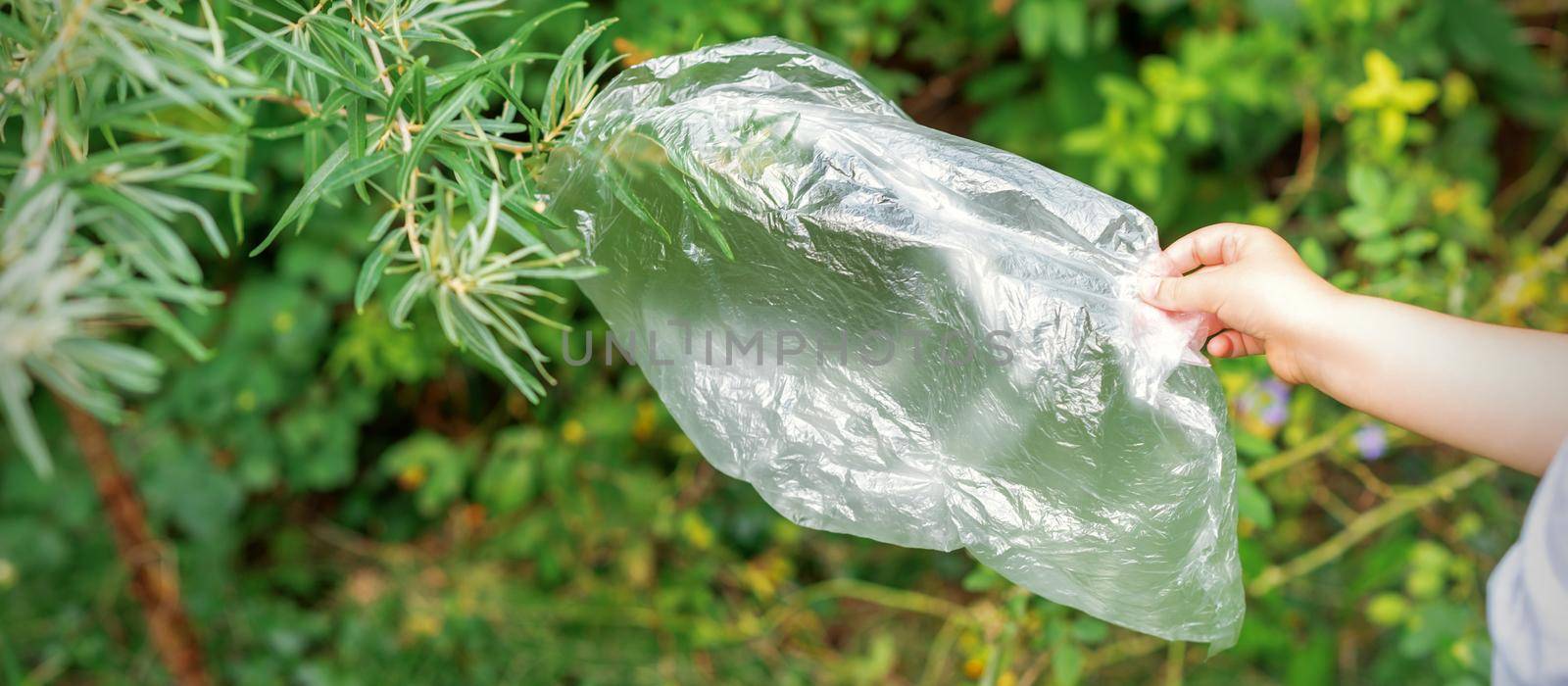 Child's hand removes the plastic bag from a branch in the park