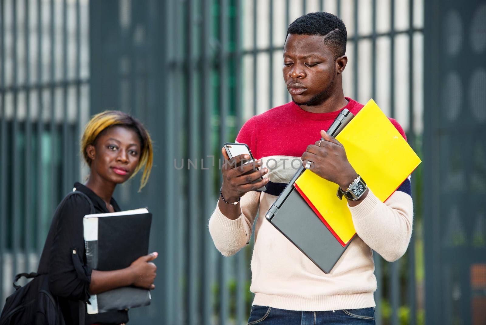 Young student using a smart phone outdoors. A serious guy looks at the phone in front of a modern building after classes.