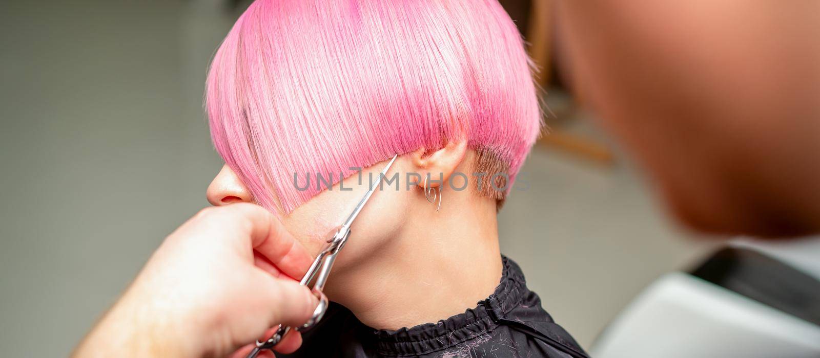 Close up of hairdresser cutting short pink hair of the young woman in a hair salon