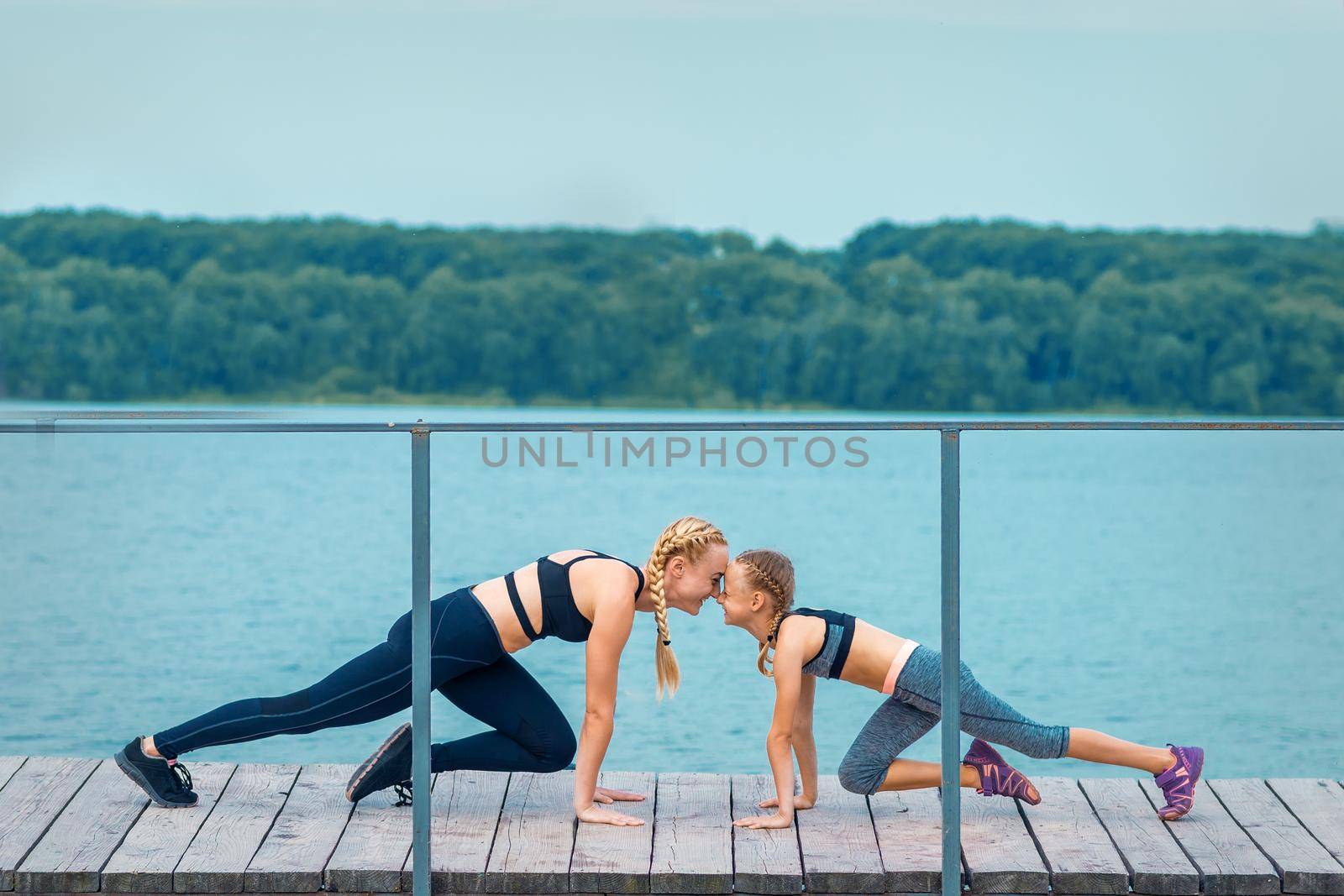 Woman and child are doing sport exercises on hands on the pier the lake