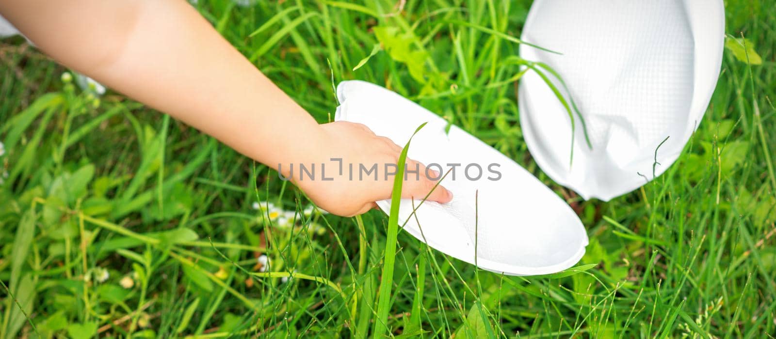 Child's hand cleans park from plastic utensils in the grass in the park