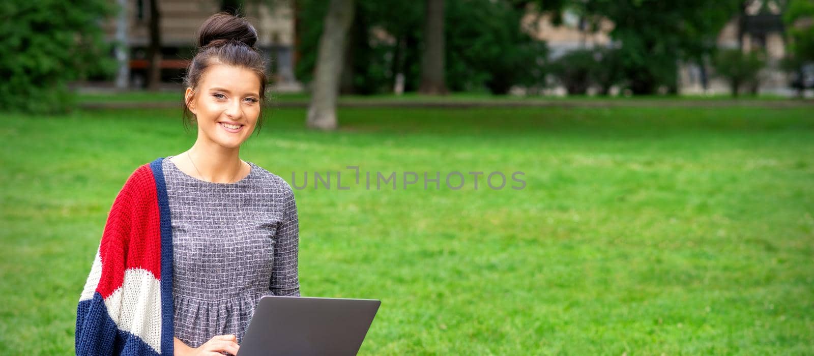 Beautiful happy young woman sitting on the bench with a laptop in the park