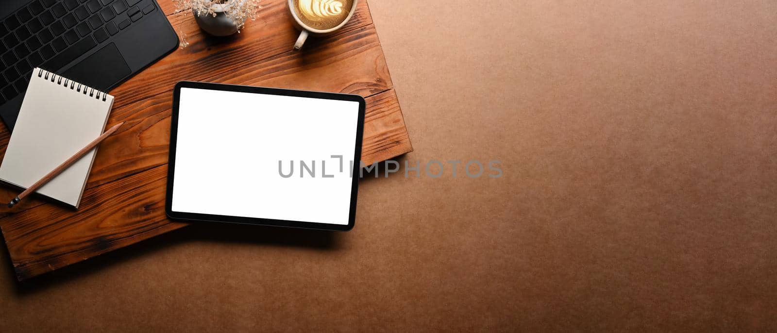 Mock up digital tablet with blank screen and laptop on brown background.