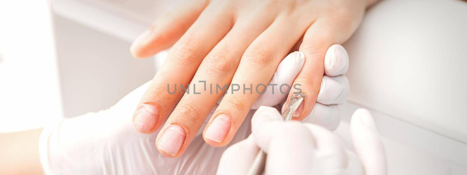 Closeup of beautiful woman's fingernails receiving cleaning cuticle with manicure pusher tool while getting a manicure