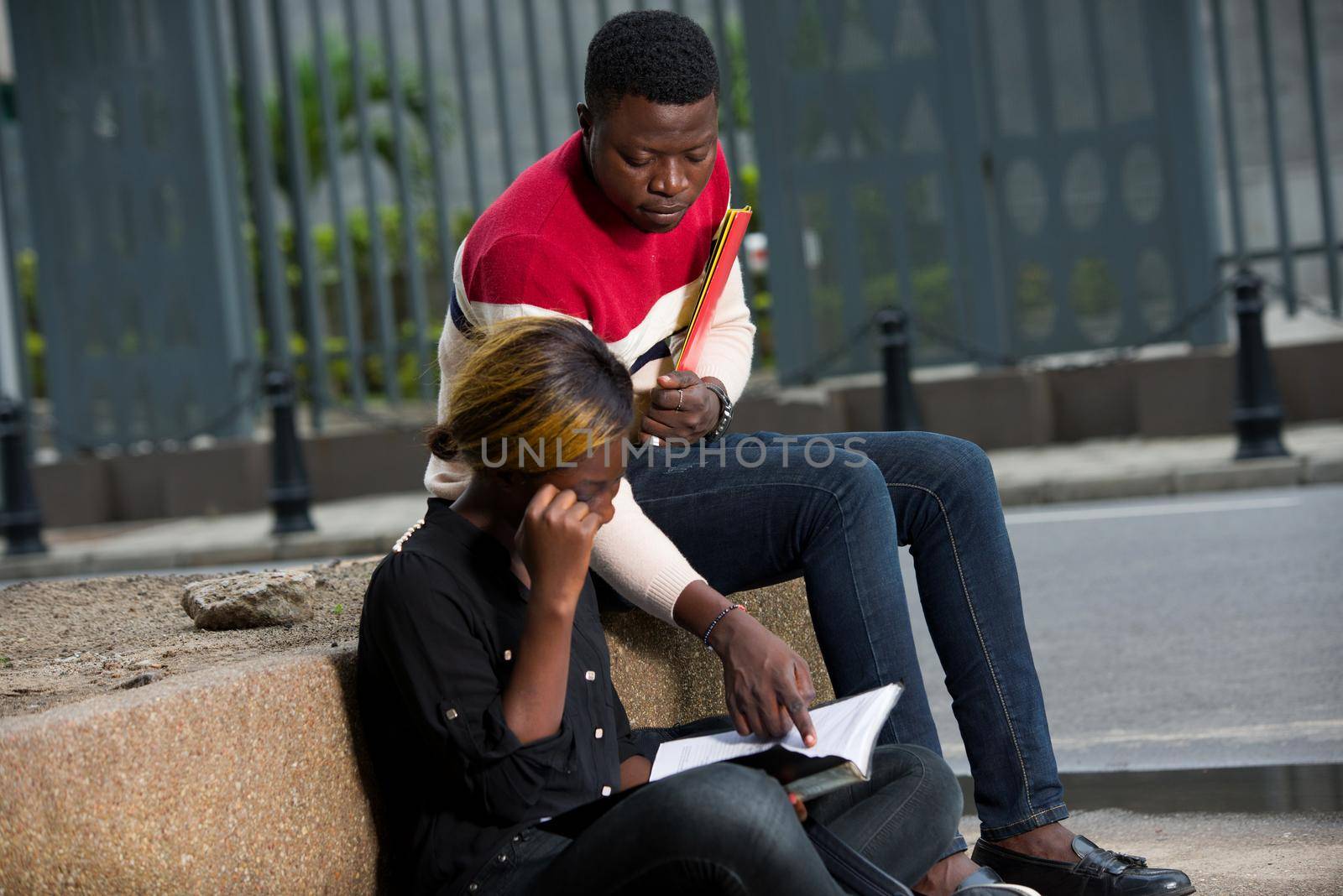 young students sitting outdoors revising class while smiling.