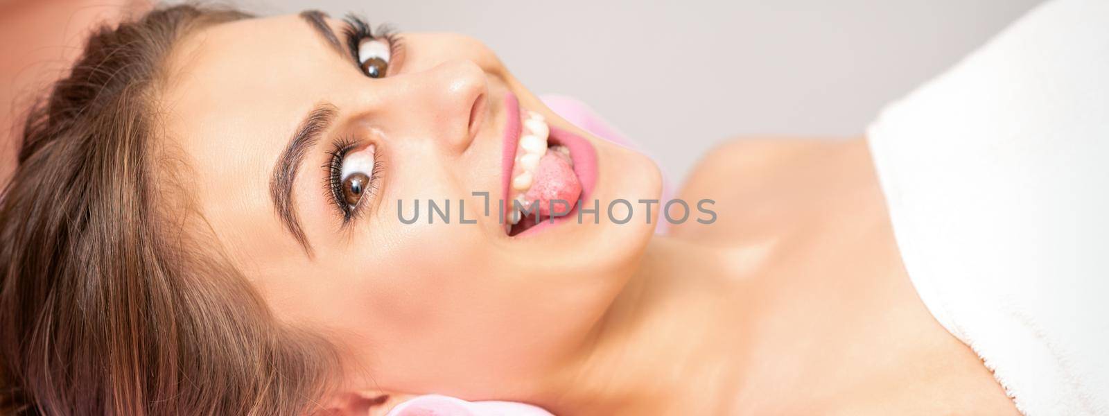 Beautiful young caucasian woman sticking out tongue and lying in spa beauty salon