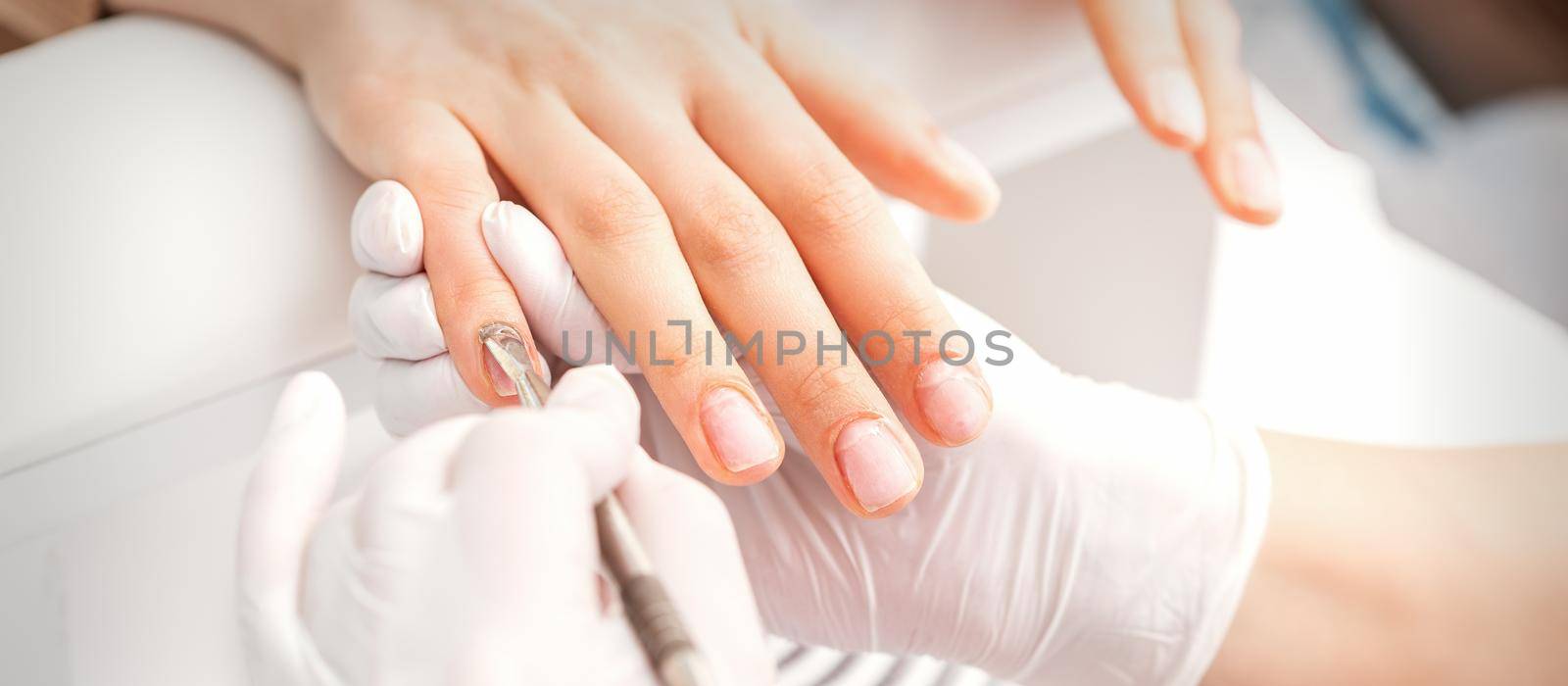 Closeup of beautiful woman's fingernails receiving cleaning cuticle with manicure pusher tool while getting a manicure