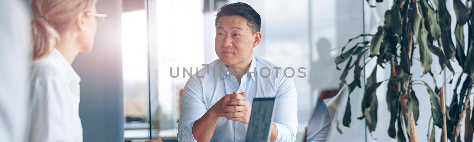 Young Asian businessman listening his colleagues on meeting in modern office by Yaroslav_astakhov