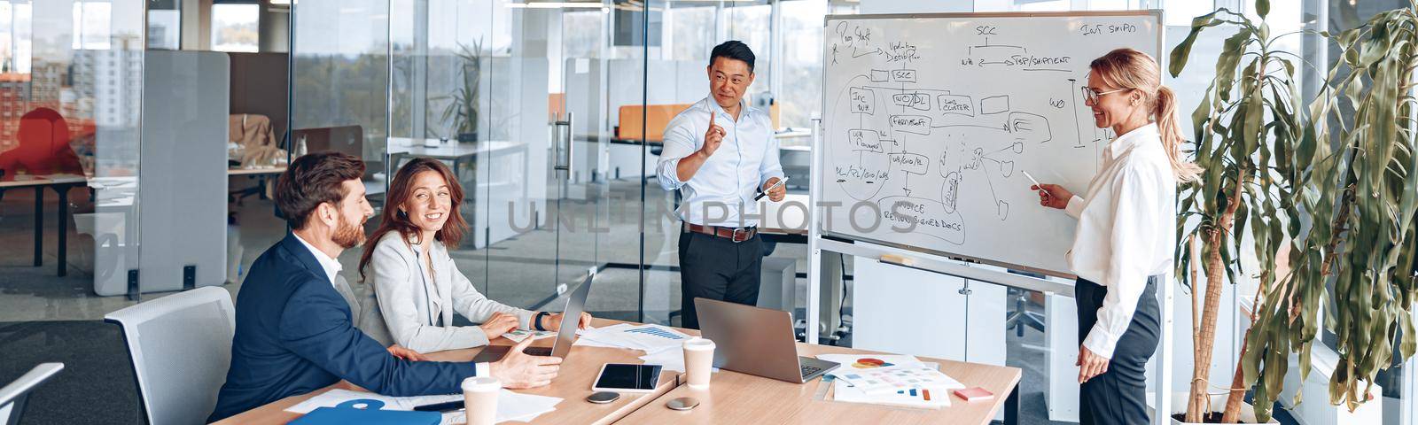 Asian man and woman conducts a meeting for employees near a flipchart and explains the work strategy by Yaroslav_astakhov