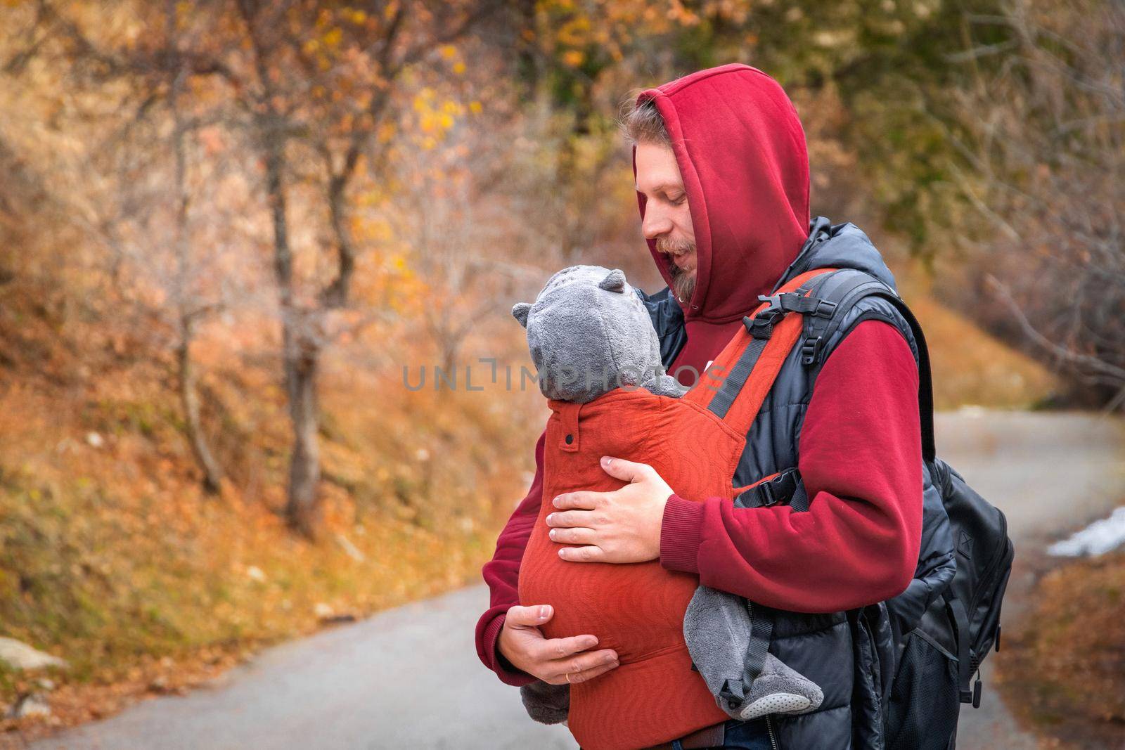 Young father with his baby boy in ergonomic baby carrier in autumn nature by Rom4ek