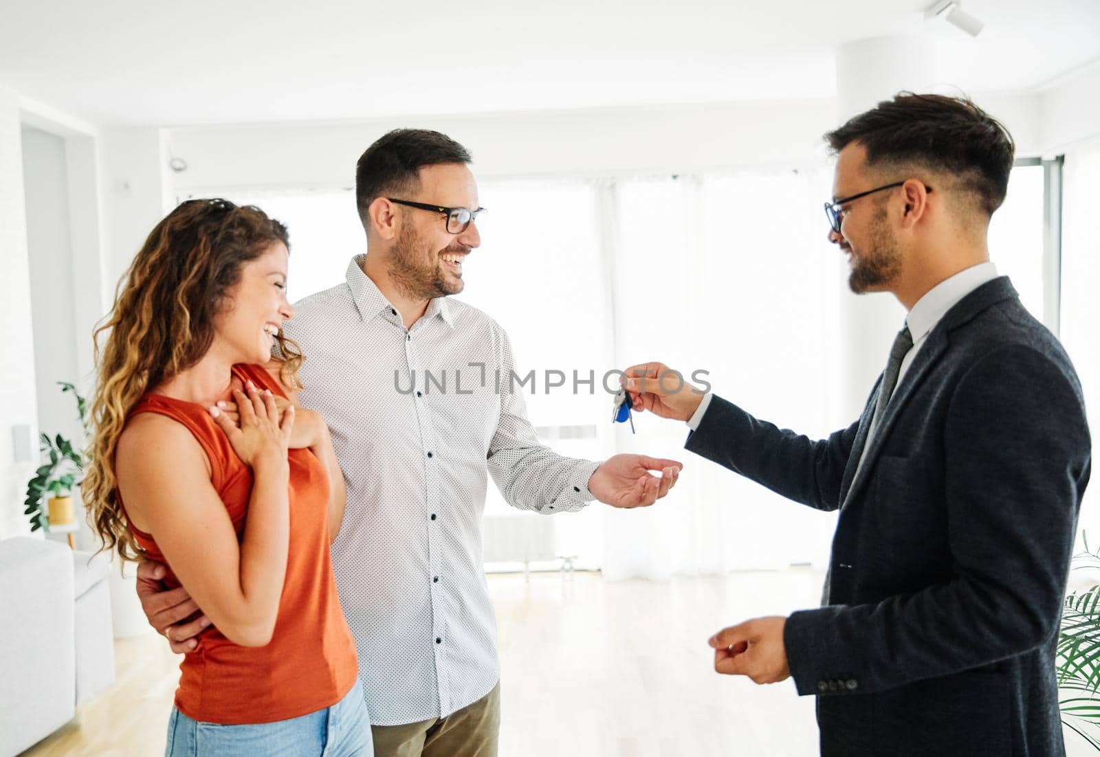 Young happy couple and an agent receiving keys of an apartment in a new real estate property