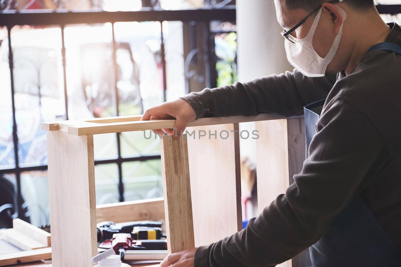 A carpenter measures the planks to assemble the parts, and build a wooden table for the customer by Manastrong